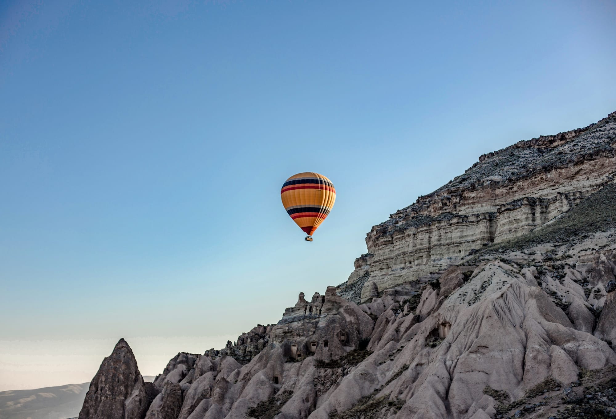 A hot air balloon floats serenely above the rugged, moon-like terrain of Cappadocia at dawn.