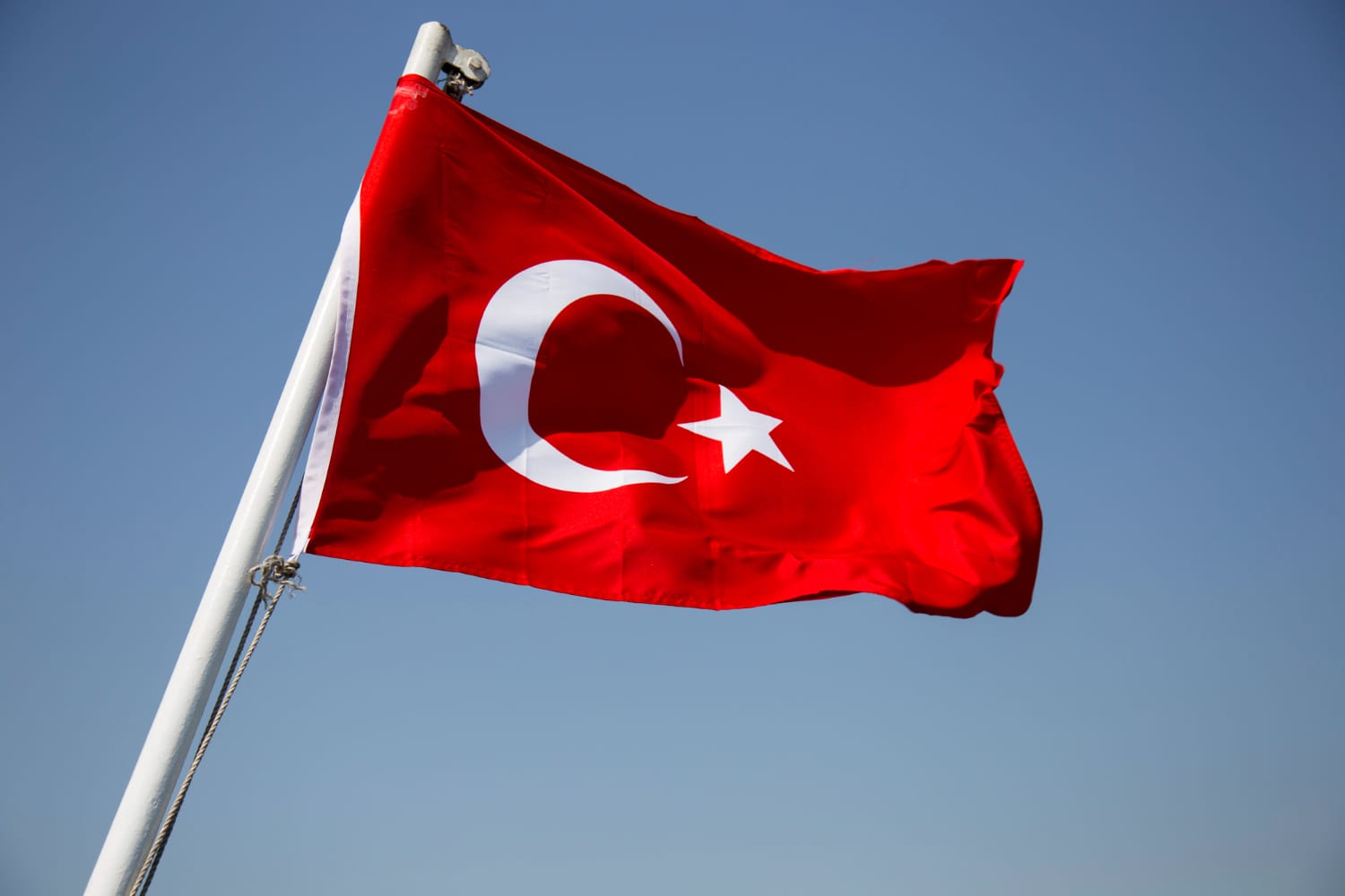 A red flag with a white star and crescent moon, the national flag of Turkey, waves against a clear blue sky—a symbol seen by many seeking residence permits Türkiye or Ikamet.