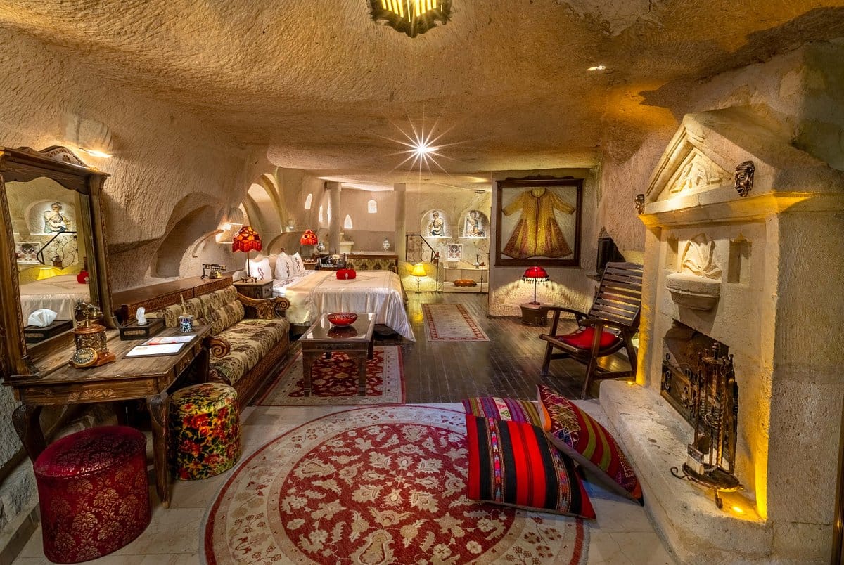 A traditionally decorated cave hotel room with carved walls, ornate furniture, and a cozy fireplace.